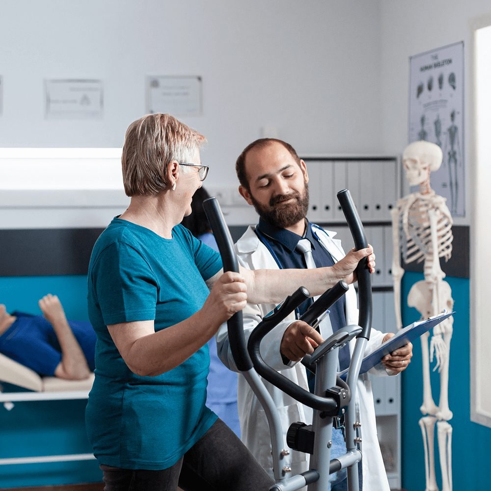 Paciente en bicicleta elíptica acompañada por un especialista en rehabilitación cardiaca